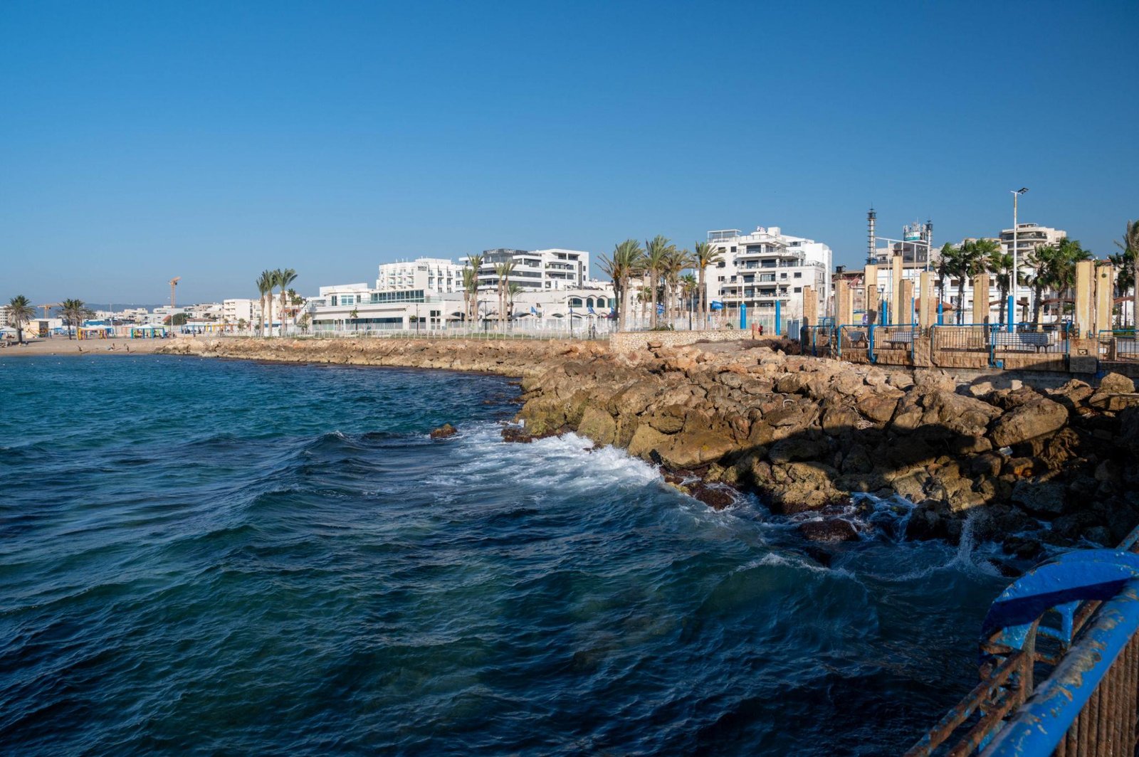 מבט רחב על העיר נהריה, המציג את קו החוף הכחול, את הטיילת השוקקת ואת מבני המגורים המשתלבים בנוף העירוני.
