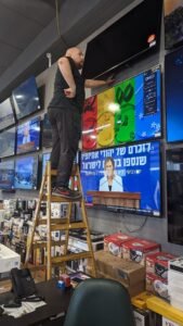 טכנאי מתקין מתקן תלייה לקיר תצוגה בחנות קמעונאית תוך סימון וקדיחה מדויקת בקיר