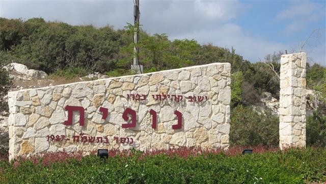 נופית יישוב קהילתי שלט כניסה על חומה עם נוף ירוק מסביב