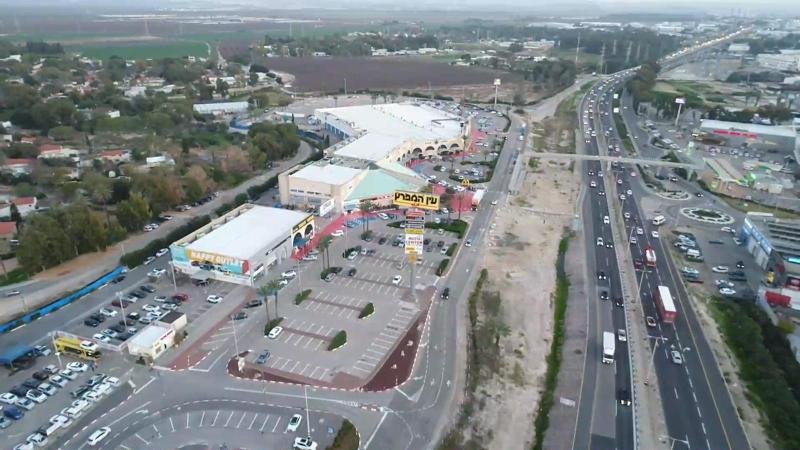 מבט רחב על מתחם ביג עין המפרץ הכולל חזיתות חנויות ושילוט של רשתות מובילות ביום שמשי.