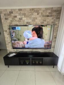 התקנת מסך 85 אינץ' על קיר בריקים מעל מזנון שחור מעוצב, ביצוע מקצועי בקרית מוצקין