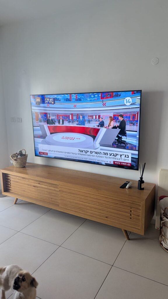 התקנת מסך 75 אינץ' על זרוע מתכווננת בקיר איטונג מעל מזנון חום כרמל, עבודה מקצועית בחיפה.